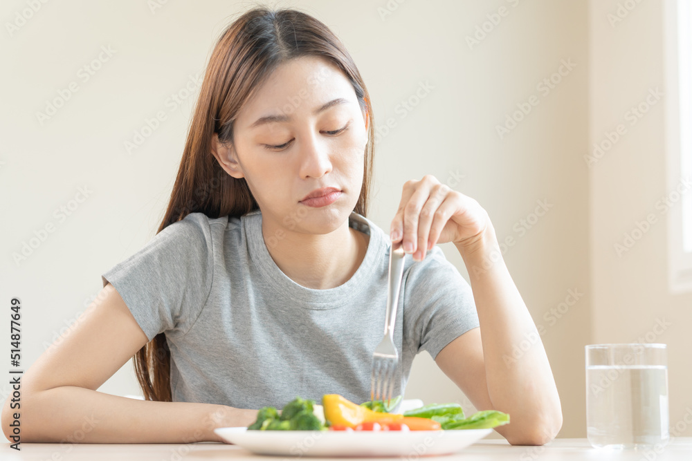 Diet in bored face, unhappy beautiful asian young woman, girl on dieting, holding fork in salad plate, dislike or tired with eat fresh vegetables. Nutrition of clean, healthy food good taste. Diet in bored face, unhappy beautiful asian young woman, girl on dieting, holding fork in salad plate, dislike or tired with eat fresh vegetables. Nutrition of clean, healthy food good taste.
