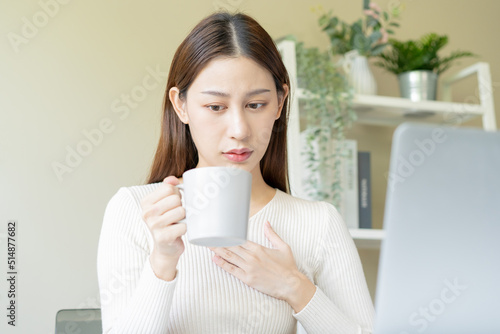 Palpitation, suffer asian young woman holding mug, drinking strong a cup of coffee, touching her chest after drink caffeine, tea while working from home, face expression stress, illness people.
