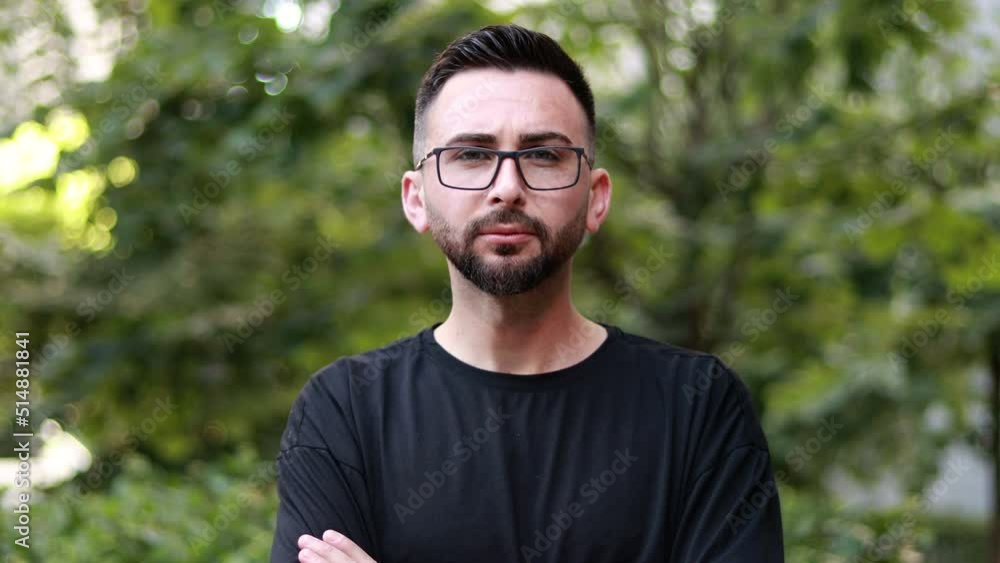 Portrait of young handsome man with beard and glasses. Young man in black shirt smiling looking at camera. Outdoor nature background Portrait of young handsome man with beard and glasses. Young man in black shirt smiling looking at camera. Outdoor nature background