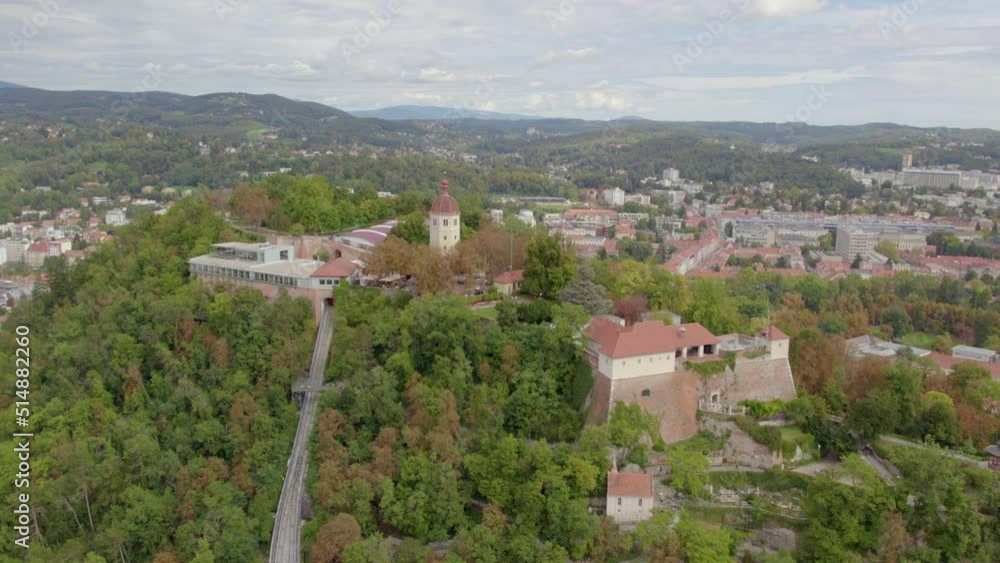Aerial view wide orbit around historic hilltop Glokenturm tower on Graz's Schloßberg with views across the city skyline Aerial view wide orbit around historic hilltop Glokenturm tower on Graz's Schloßberg with views across the city skyline