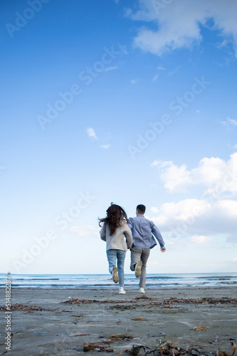 Young couple from behind is running at the beach to the sea in Larnaca, Cyprus