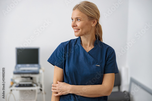 Smiling doctor, ultrasound specialist looking at side on her workplace in clinic