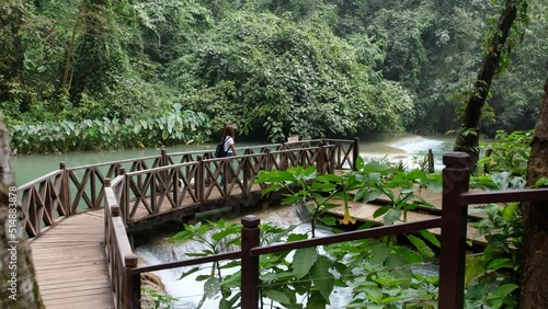 A female traveler and a dog walking on a red bridge by The Tat Kuang Si waterfall in Luang Prabang, Laos