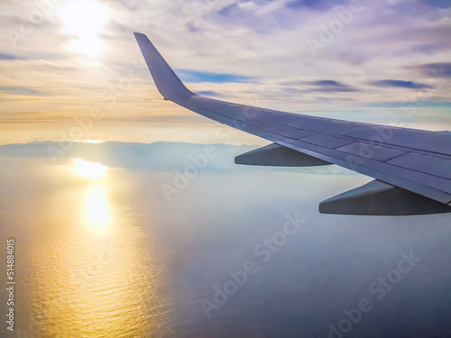 View from the plane window on the island of Tenerife in the Atlantic Ocean at dawn. The wing of an airplane flying under the clouds over the Canary Islands and the reflection of the sun in the water