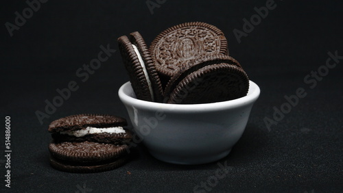 A bowl of Cookies isolated on black background. Chocolate cookies with white cream filling on white bowl