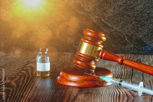 Judges hammer, syringe and vaccine bottle on a wooden background with sun light. Concept for a medical judgment
