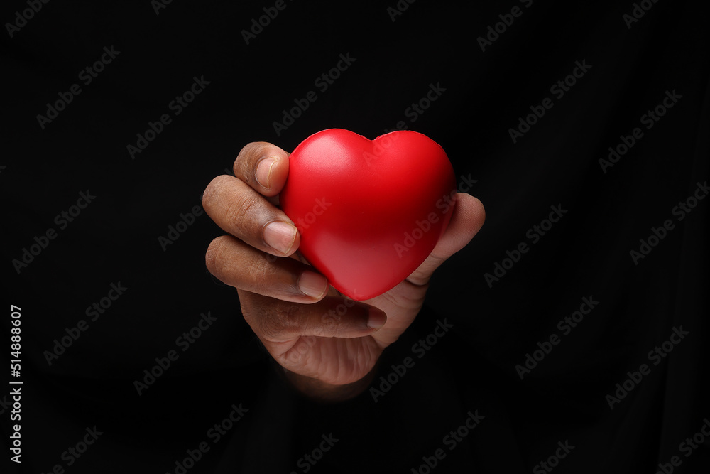 Asian male dark skinned single hand fist finger on black background holding red rubber hart love shape Asian male dark skinned single hand fist finger on black background holding red rubber hart love shape