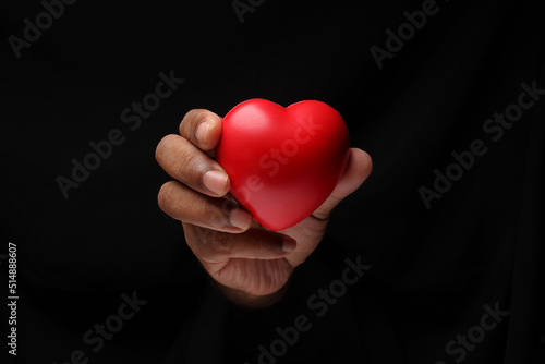 Asian male dark skinned single hand fist finger on black background holding red rubber hart love shape