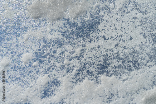 Texture of frozen street glass with abstract patches of hoarfrost and snow against a blue sky. Close-up.