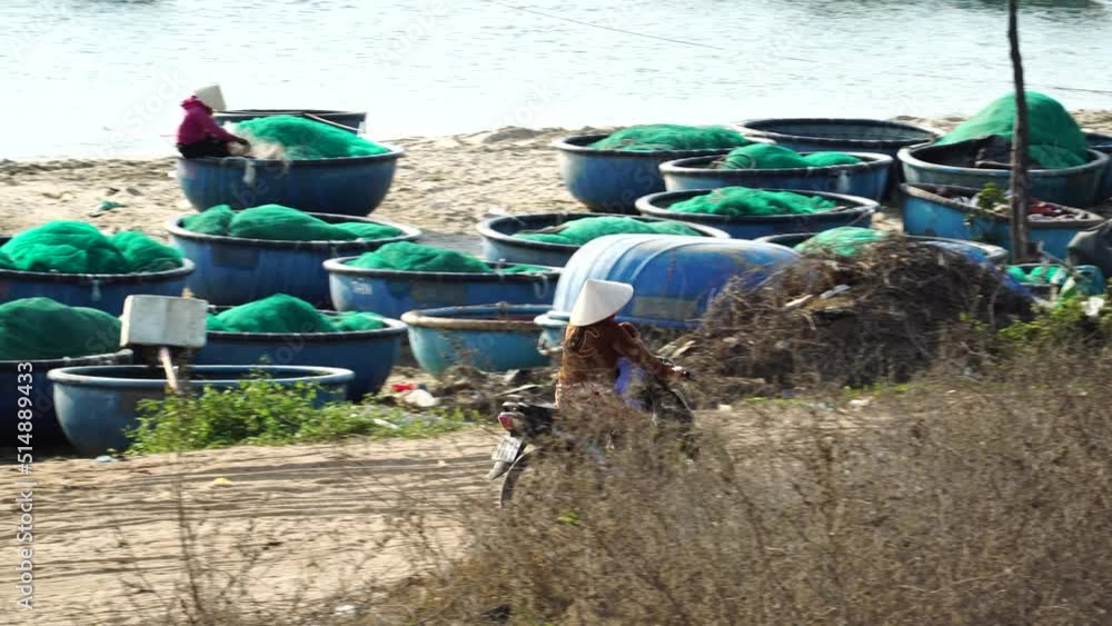 Vietnamese woman with child riding motorbike, beach with coracle boats. Tracking shot Vietnamese woman with child riding motorbike, beach with coracle boats. Tracking shot