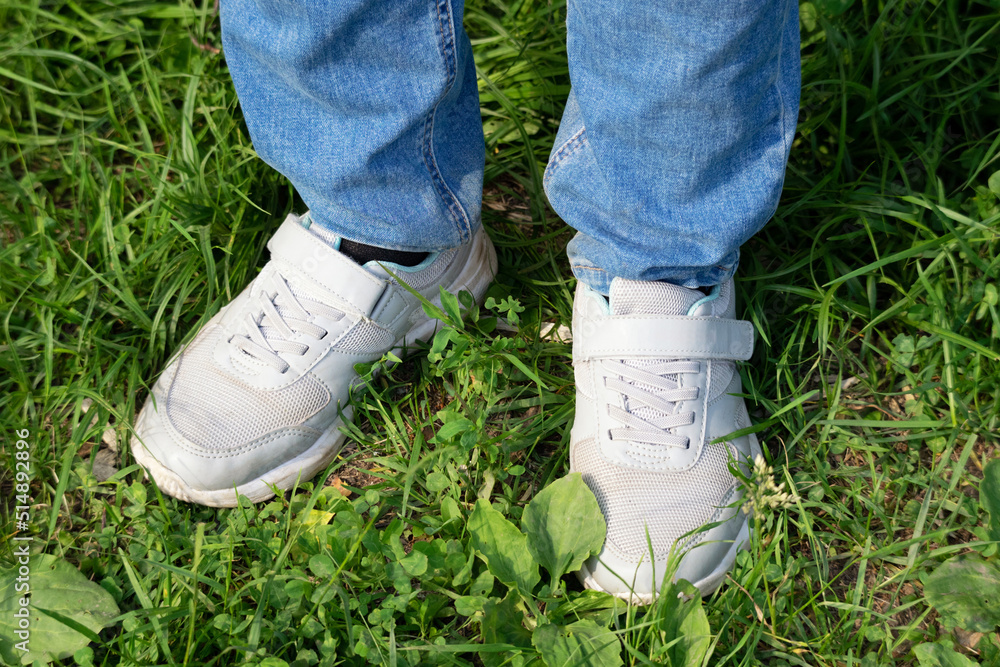 Young woman in jeans and gray sneakers in the forest on a clearing in the grass Young woman in jeans and gray sneakers in the forest on a clearing in the grass