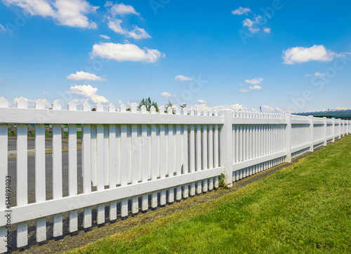White wooden fence on the blue sky background. Green lawn and wooden white fence on sunny summer day