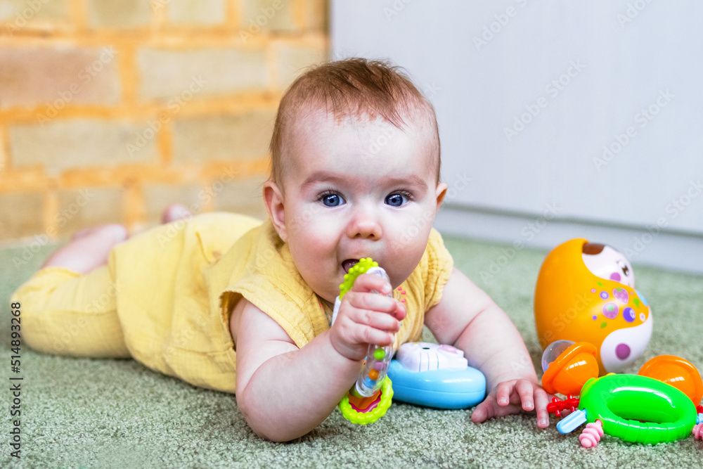 Cute little baby girl lying on a floor and playing with colorful plastic and wooden toys. Develop of child motor skills. Cute little baby girl lying on a floor and playing with colorful plastic and wooden toys. Develop of child motor skills.