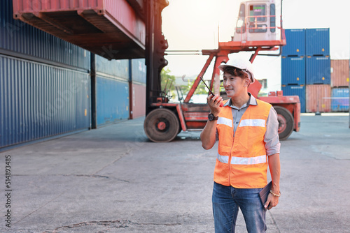 Foreman using walkie talkie radio and tablet control loading containers box. Engineer or worker with safety hat work at container cargo site and checking industrial container cargo freight ship.