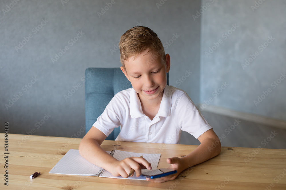 Cute boy writes in an open notebook and looks at the phone. Cute boy writes in an open notebook and looks at the phone.