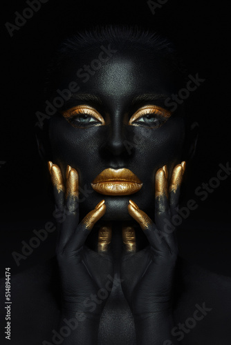 Fotografia Beauty woman painted in black skin color body art, gold makeup lips eyelids, fingertips nails in gold color paint