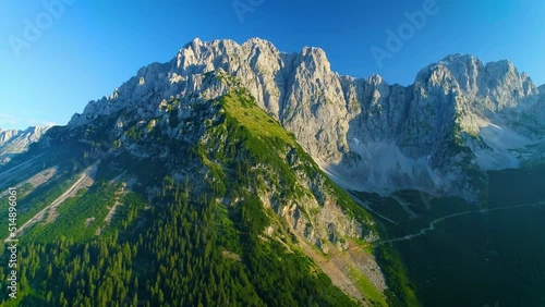 Stunning aerial view across woodland covered slopes of sunlit Wilder Kaiser mountains peaks