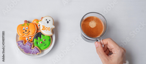woman hand holding coffee cup during eating funny Halloween Cookies. Happy Halloween day, Trick or Threat, Hello October, fall autumn, Traditional, party and holiday concept