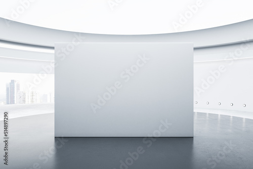Murais de parede Front view on blank on light grey partition with place for your logo or text on concrete floor in empty sunlit round gallery hall with city view