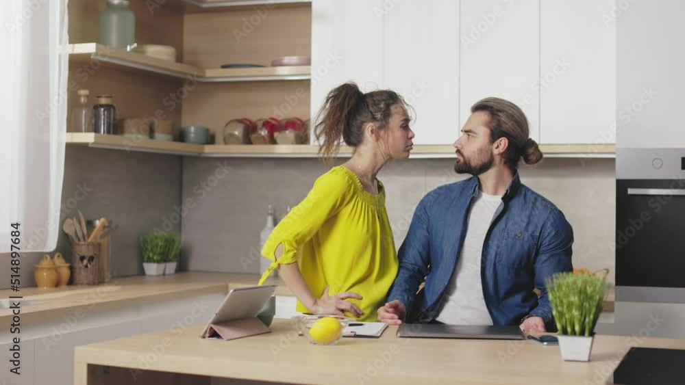 Displeased caucasian woman asking for attention from busy husband that sitting on kitchen and working on laptop. Concept of freelance, relations and understanding. Displeased caucasian woman asking for attention from busy husband that sitting on kitchen and working on laptop. Concept of freelance, relations and understanding.