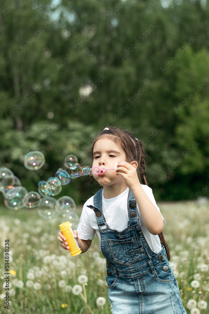 Portrait of a happy little caucasian girl blowing soap bubbles on a summer day in the park.Summer, childhood concept.