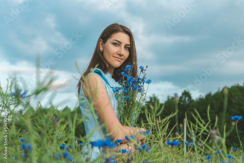 Young pretty woman among the field of beautiful cornflowers