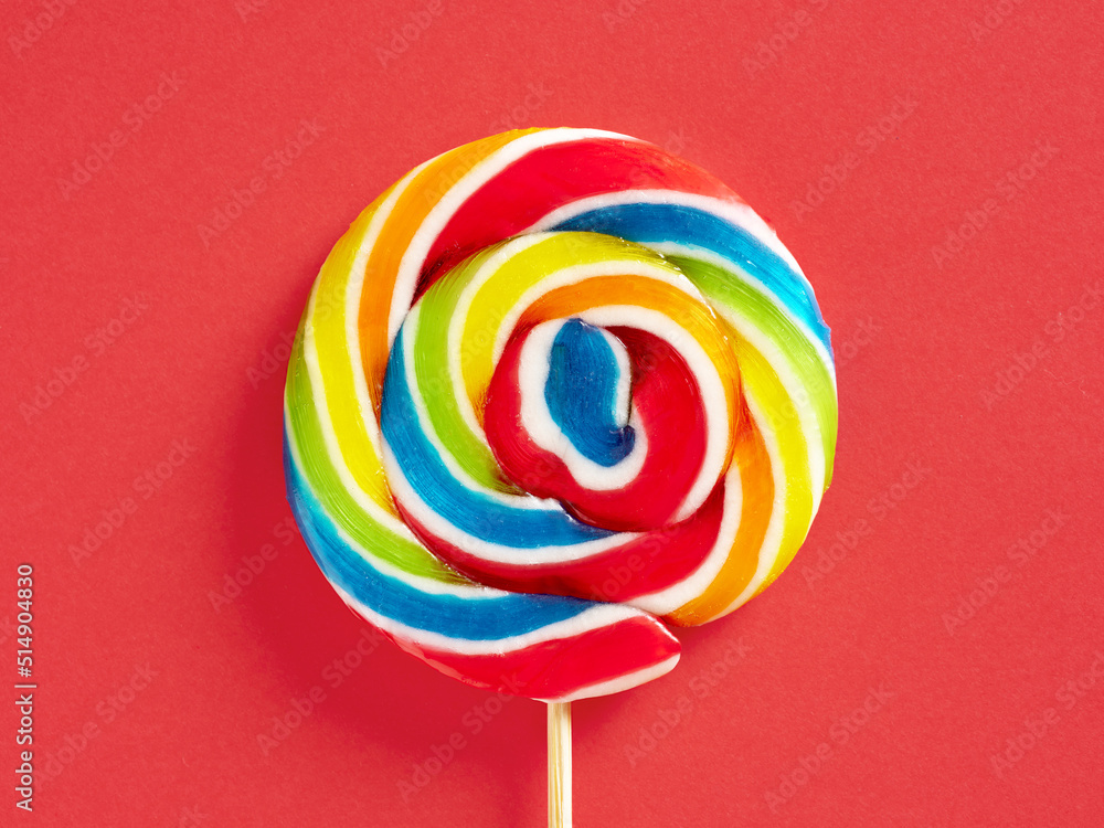 Rainbow colored swirl round candy lollipop on red background. Close up macro.