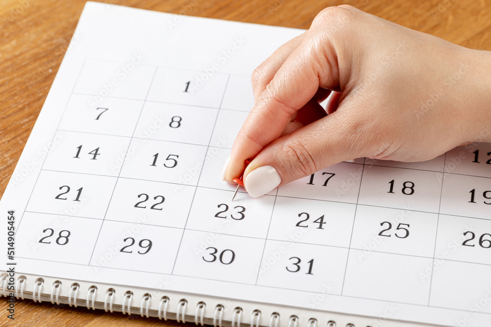beautiful female Hand with manicure pushes a red pin on a calendar 23 day beautiful female Hand with manicure pushes a red pin on a calendar 23 day