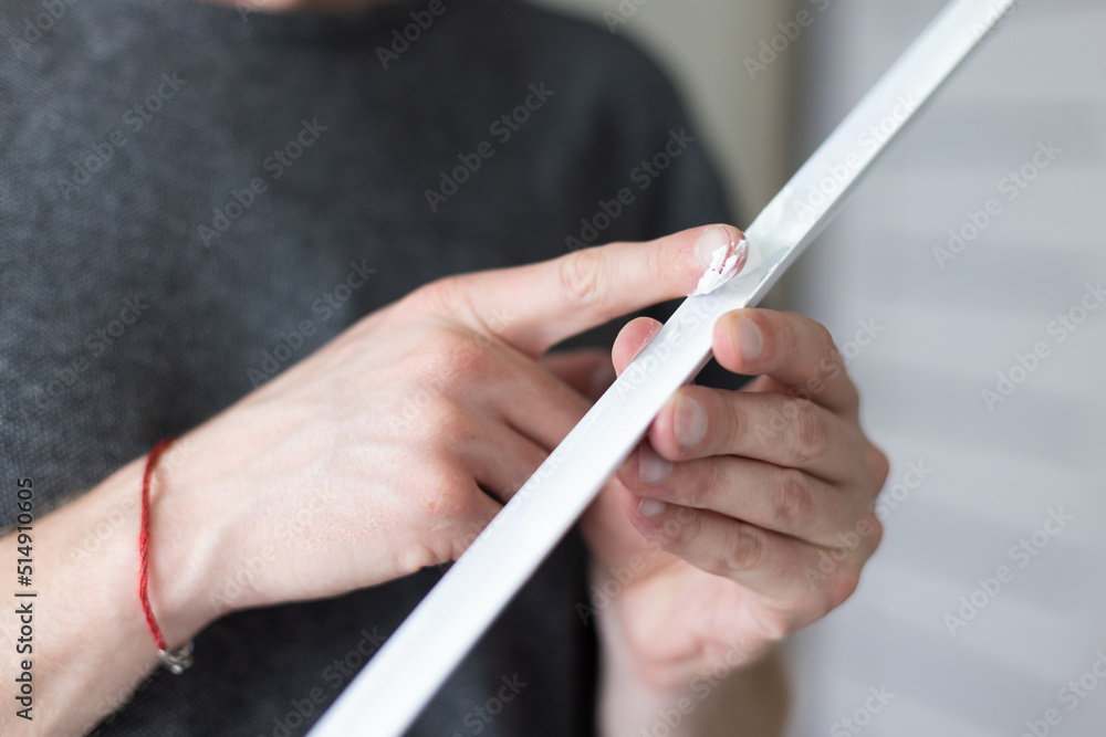 Man putting glue by finger on decorative plastic corner for the wall protection in apartment. Man putting glue by finger on decorative plastic corner for the wall protection in apartment.