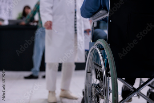 Closeup of man using wheelchair in front of medical doctor in private hospital reception for routine checkup. Selective focus on senior man living with disability at clinic reception for appointment.