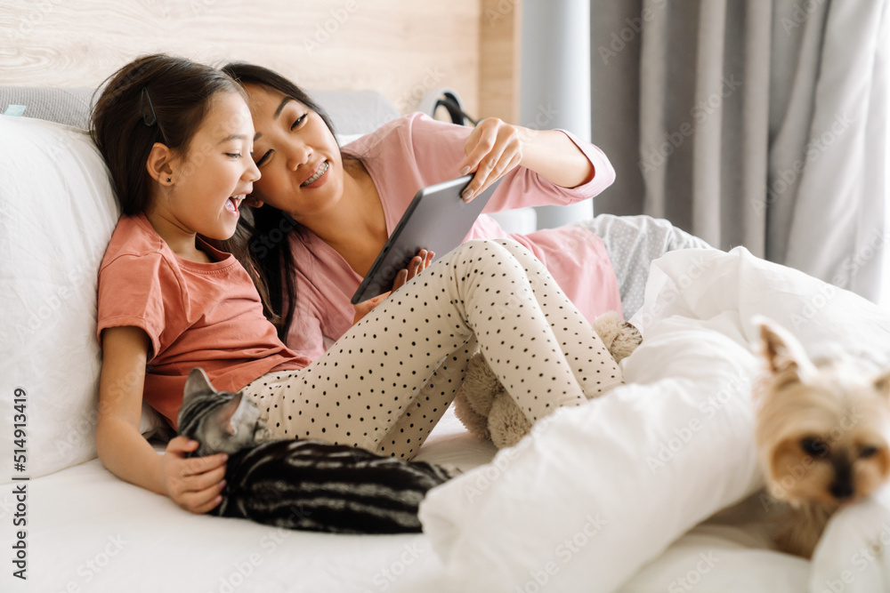 Asian mother and daughter using laptop while sitting on bed Asian mother and daughter using laptop while sitting on bed