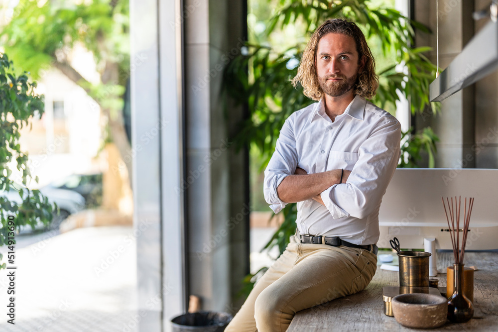 Confident executive with arms crossed sitting on table in office Confident executive with arms crossed sitting on table in office