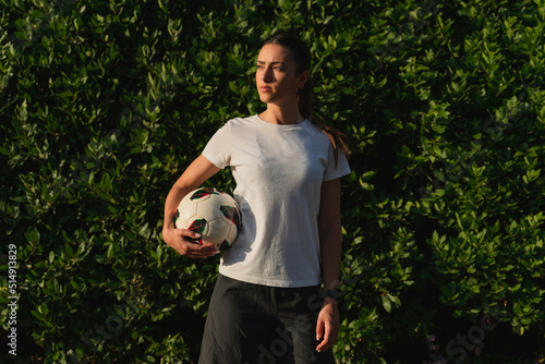Thoughtful woman with soccer ball standing in front of plants photo