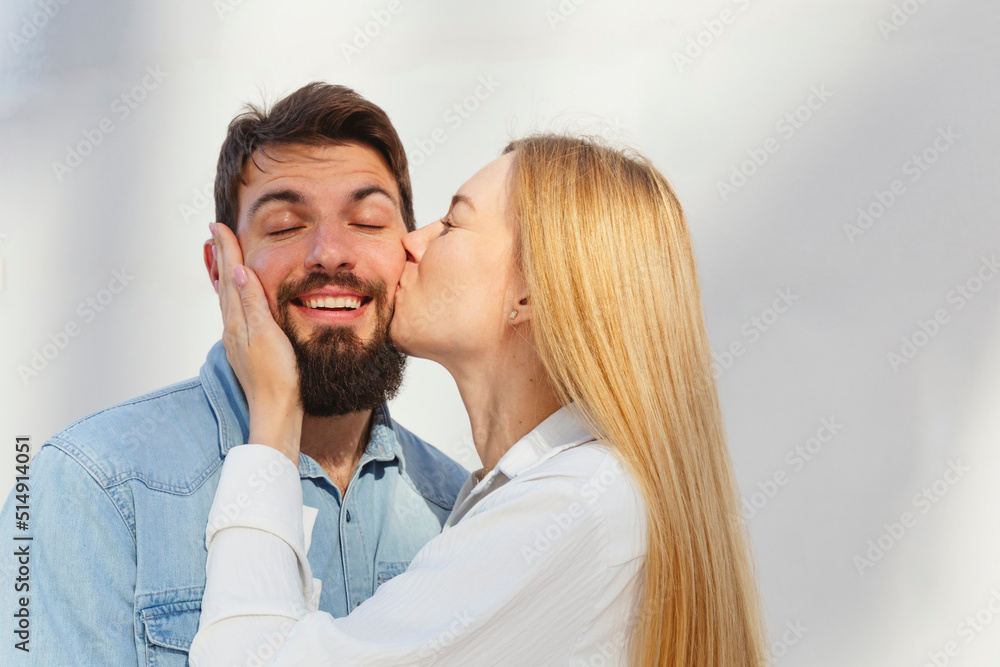 Affectionate blond woman kissing man on cheek in front of wall Affectionate blond woman kissing man on cheek in front of wall