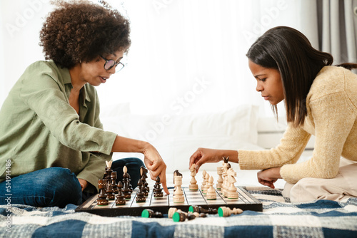 Happy african american woman and her daughter playing chess at home