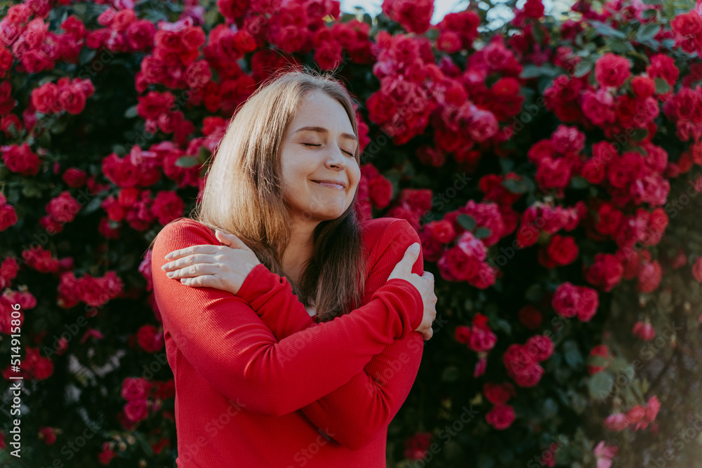 Smiling woman hugging self in front of rose plant Smiling woman hugging self in front of rose plant