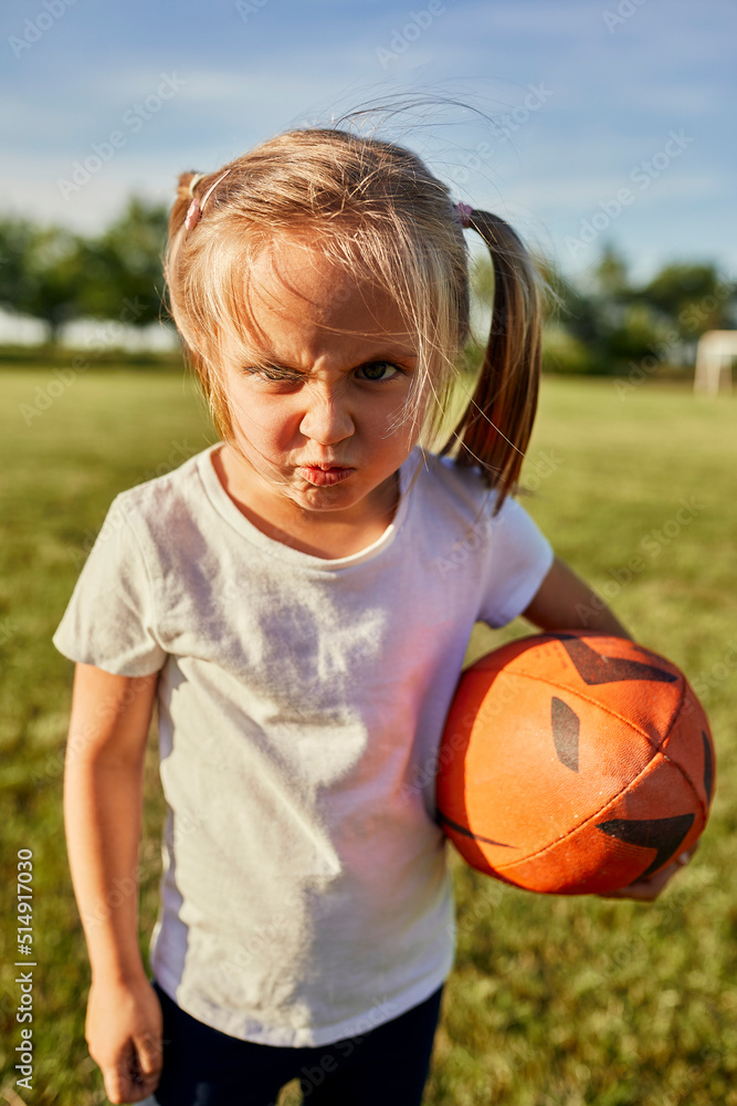 Blond girl with rugby ball making face at sports field on sunny day Blond girl with rugby ball making face at sports field on sunny day