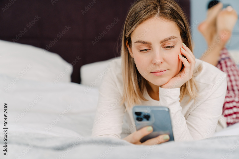 Young white blond woman using cellphone while lying in bed at home Young white blond woman using cellphone while lying in bed at home