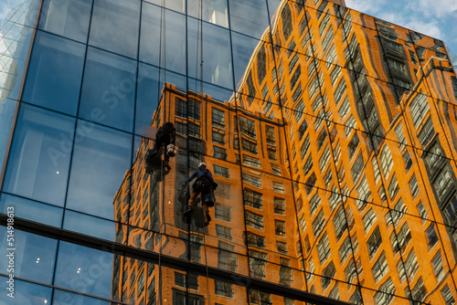 Washers wash skyscraper windows sitting on hanging seats. Industrial climbers wash the windows of a modern skyscraper. Men wash Windows on the evolution tower. Workers cleaning office building windows
