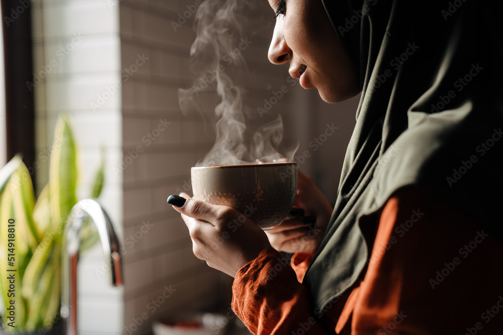 Young calm woman in hijab holding cup of hot tea - obrazy, fototapety, plakaty 
