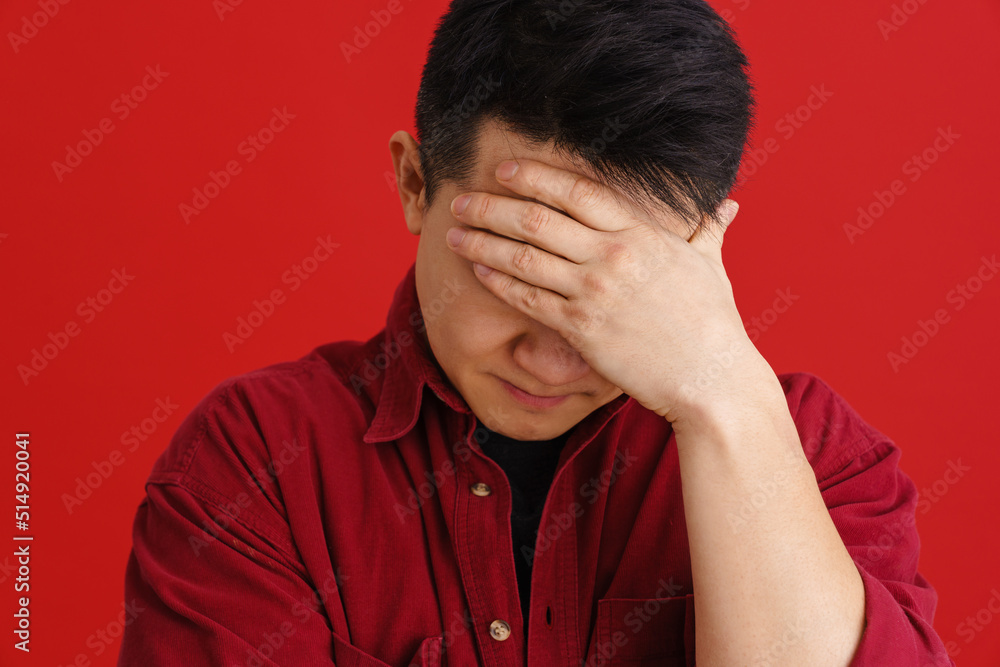 Asian puzzled man holding his forehead while posing on camera Asian puzzled man holding his forehead while posing on camera