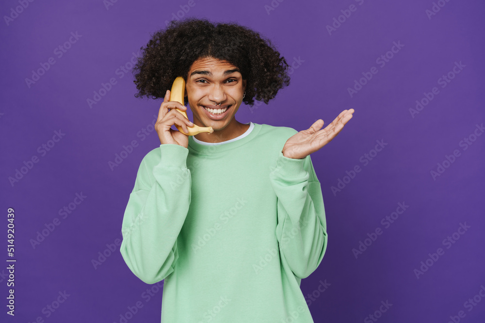 Young smiling curly latin man talking on banana like phone Young smiling curly latin man talking on banana like phone