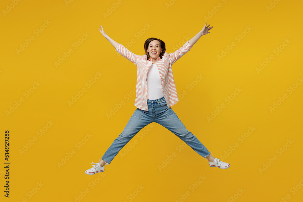 Full body young happy exultant jubilant fun woman she 30s wears striped shirt white t-shirt jump high with outstretched hands legs isolated on plain yellow background studio. People lifestyle concept.