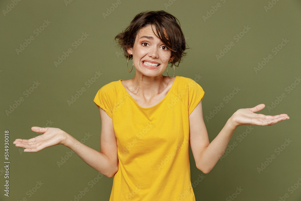 Young woman she 20s wear yellow t-shirt shrugging shoulders looking puzzled, have no ideastanding questioned and unaware, I don't know, why spread hands isolated on plain olive green khaki background. Young woman she 20s wear yellow t-shirt shrugging shoulders looking puzzled, have no ideastanding questioned and unaware, I don't know, why spread hands isolated on plain olive green khaki background.