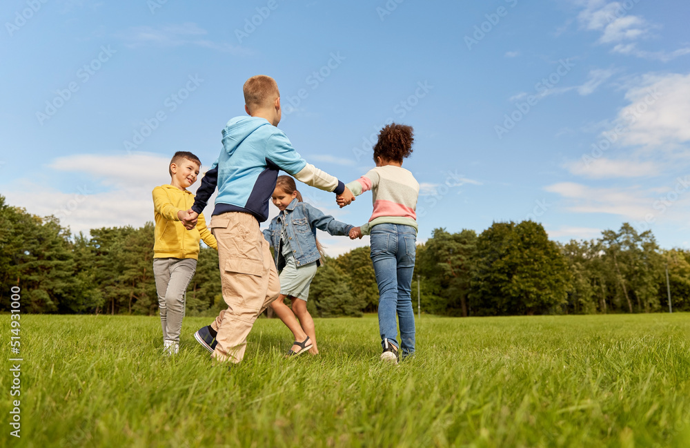 childhood, leisure and people concept - group of happy kids playing round dance at park