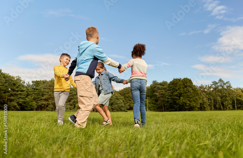 childhood, leisure and people concept - group of happy kids playing round dance at park © Syda Productions