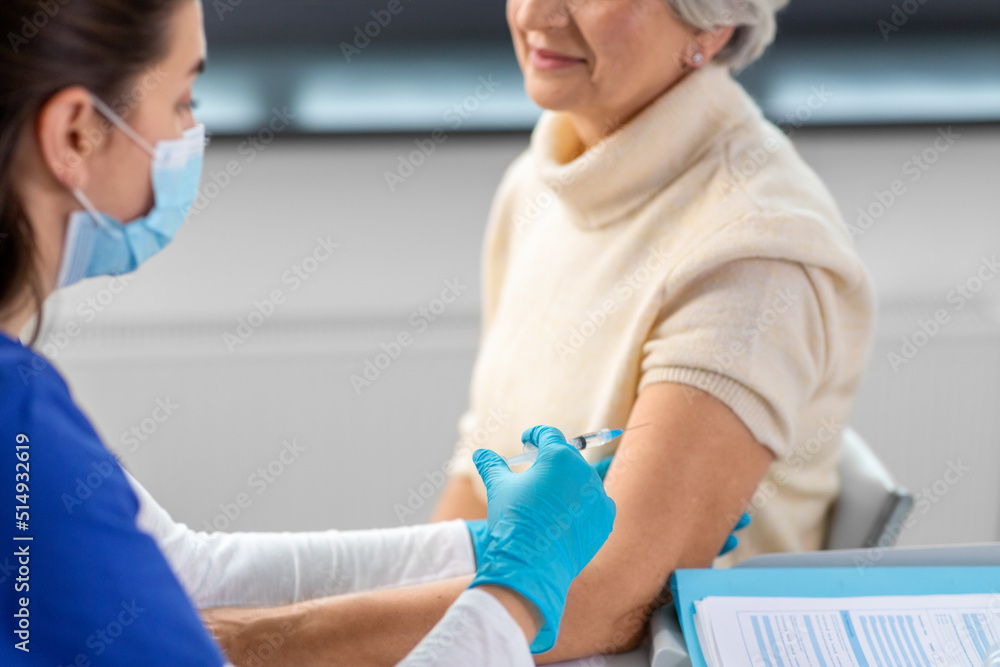 medicine, health and vaccination concept - close up of doctor or nurse with syringe making vaccine or drug injection to senior woman in mask at hospital medicine, health and vaccination concept - close up of doctor or nurse with syringe making vaccine or drug injection to senior woman in mask at hospital