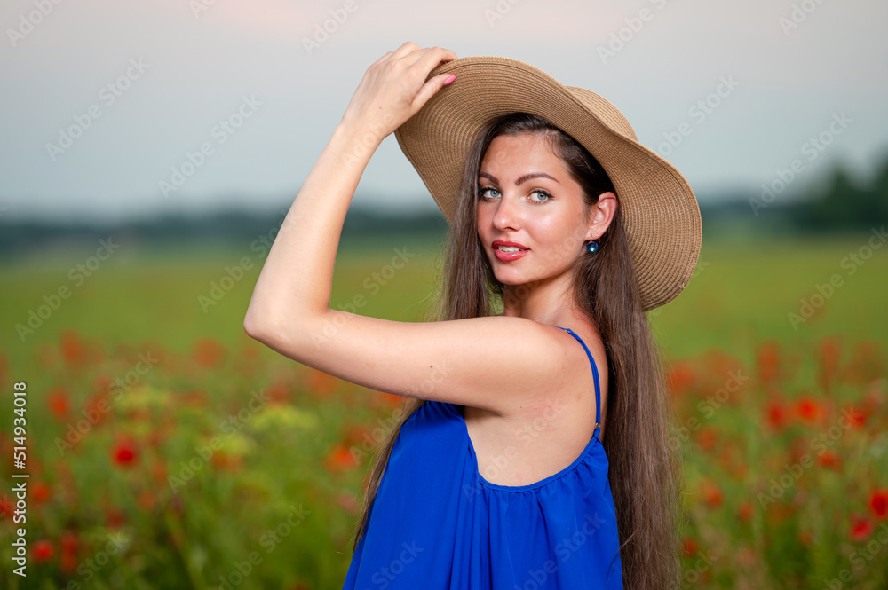 portrait of young woman with long hair and straw hat in poppy field in evening sunlight