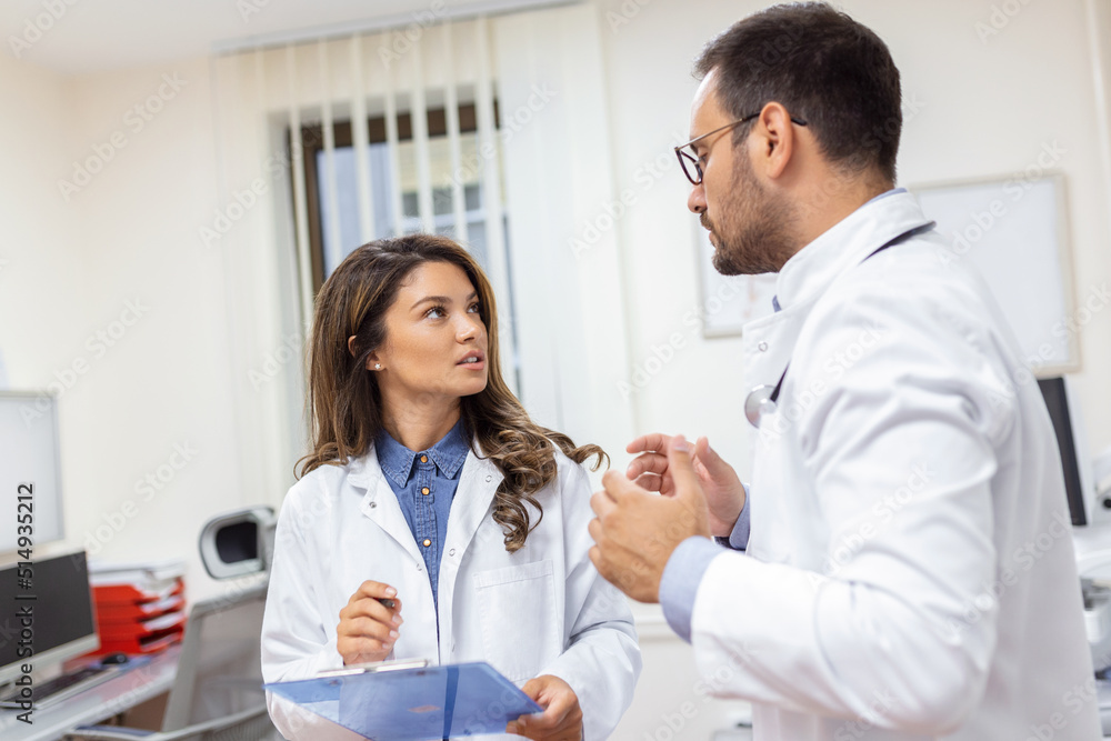 Fototapeta premium Doctors discussing over a medical report in hospital. Female and male doctor checking clinical report of patient online. Healthcare staff having discussion in a office of private clinic.