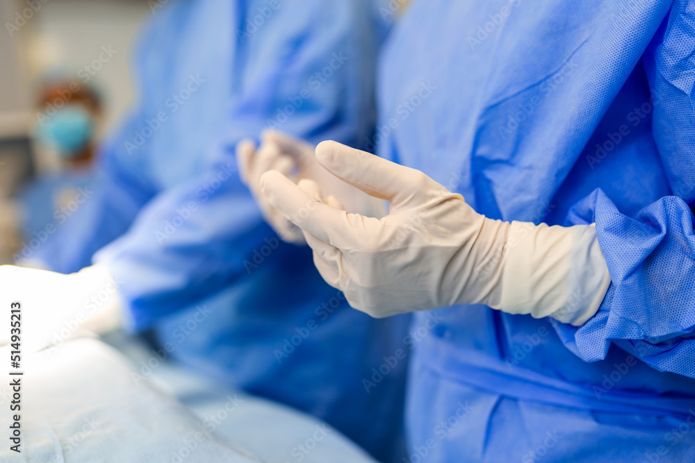 Portrait of beautiful female doctor surgeon putting on medical gloves standing in operation room. Surgeon at modern operating room